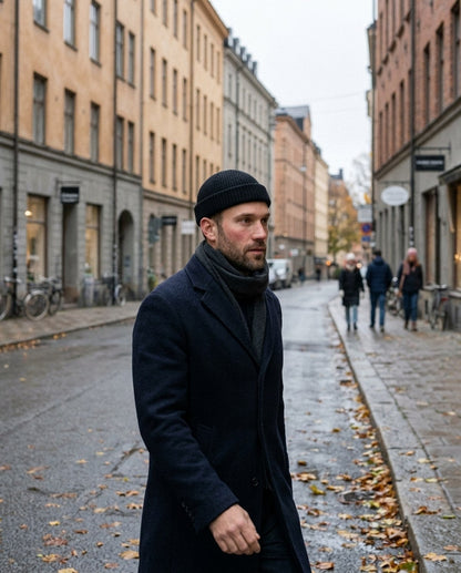Mann i svart fisherman-lue og marineblå frakk i en bygate